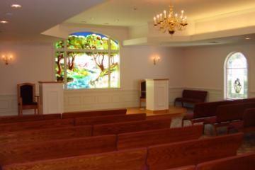 Empty church sanctuary with wooden pews and stained-glass windows, softly lit by chandeliers