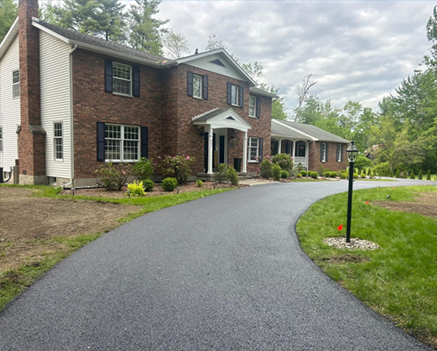Asphalt driveway leading to a two-story brick house with a white columned entryway.