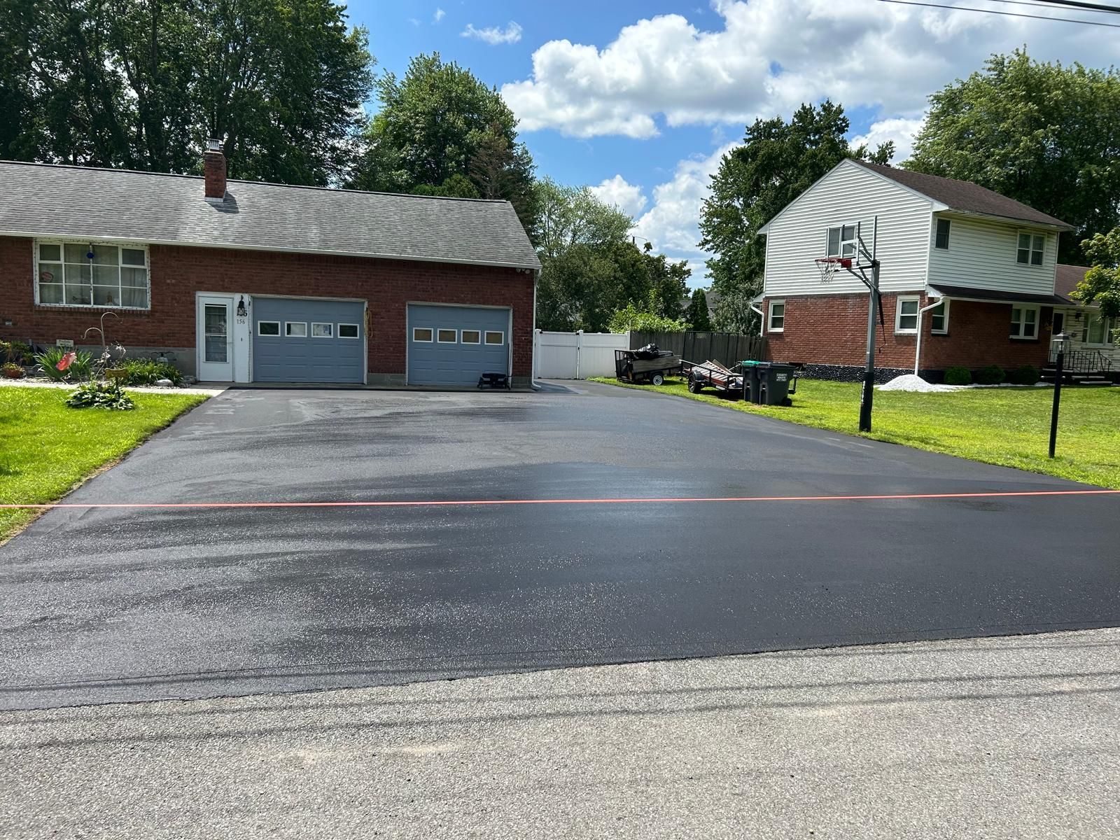 Newly paved asphalt driveway in front of a brick house with a garage and a two-story house.