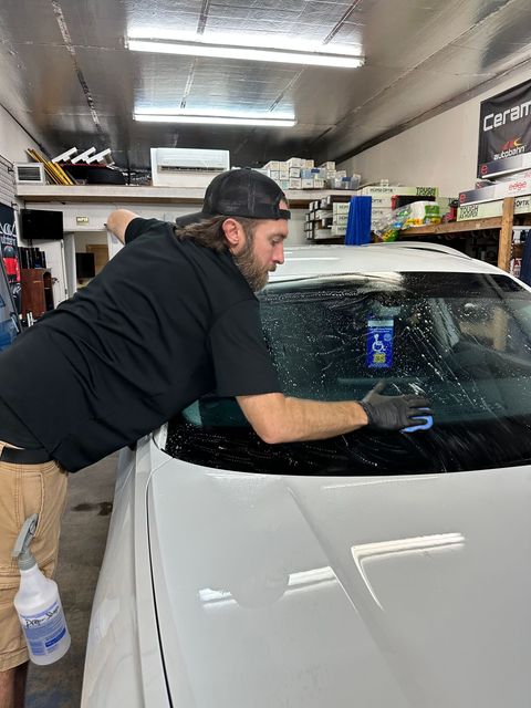 Man cleaning the windshield of a white car in a garage