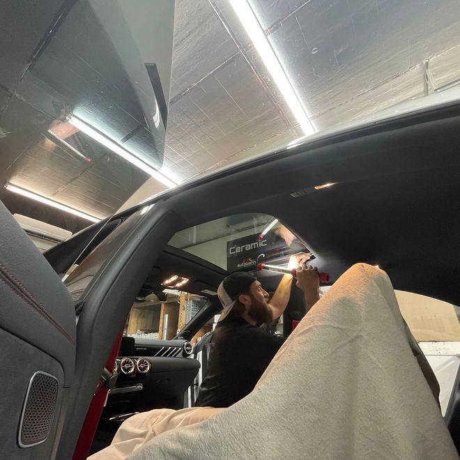 A person is using a blue squeegee to remove plastic from the hood of a car