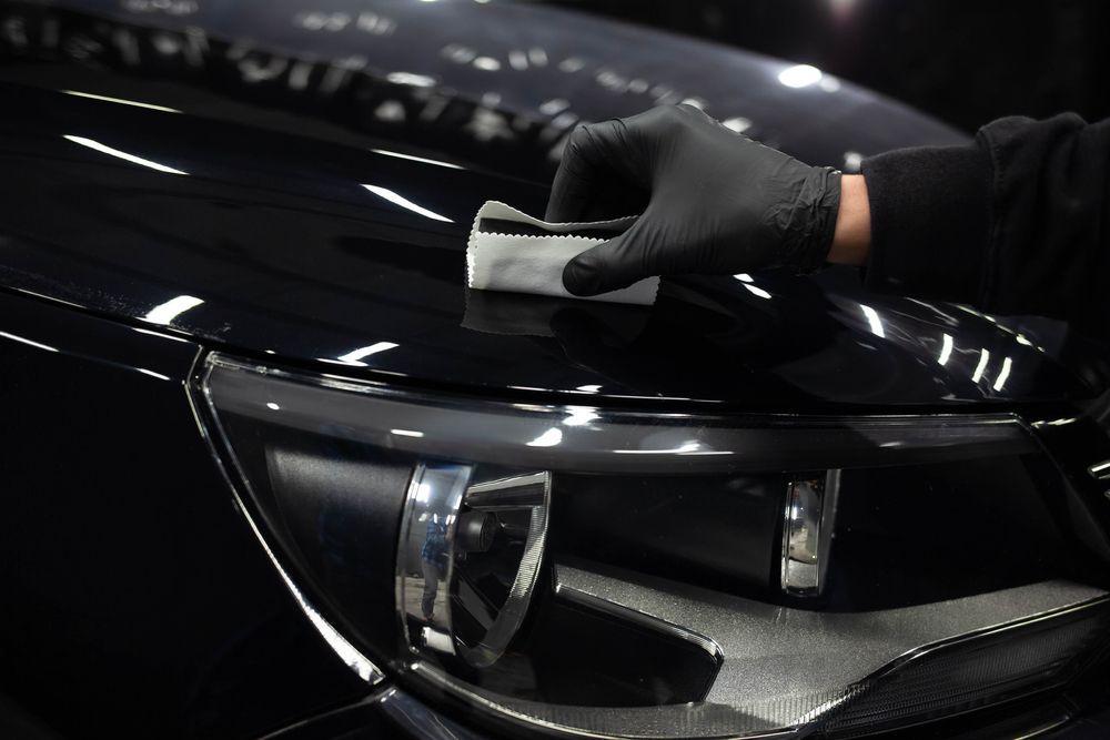 A person is polishing the hood of a black car.