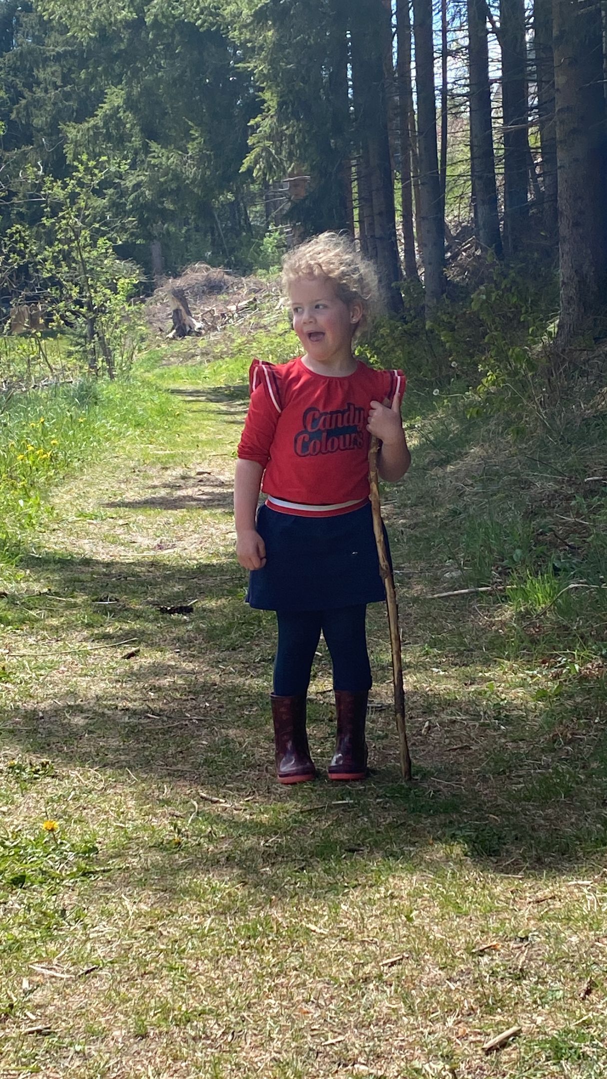 Een klein meisje staat in het gras met een stok in haar handen.