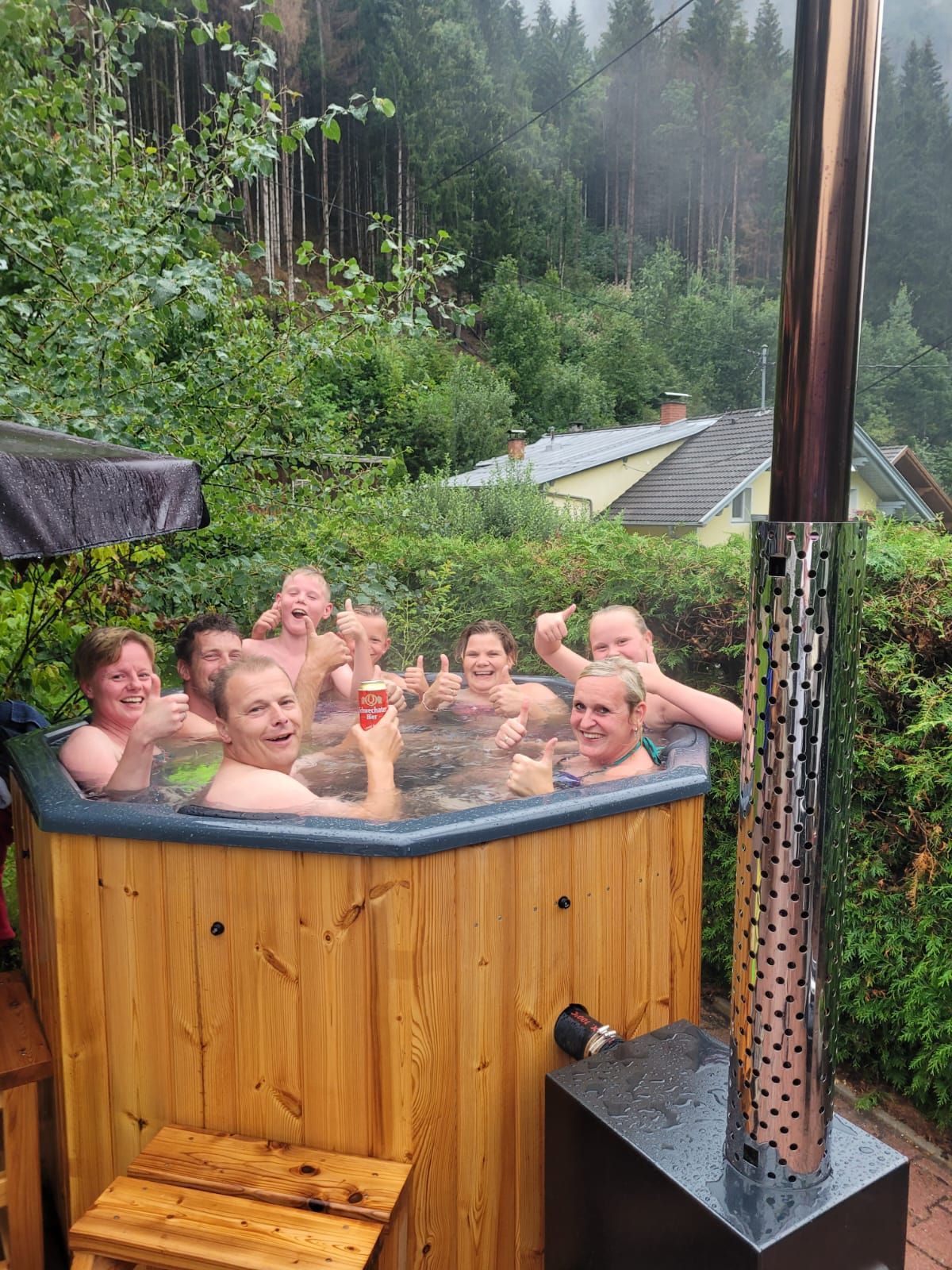 Menschen entspannen sich in einem hölzernen Whirlpool im Freien inmitten dichter Vegetation und Bäume.