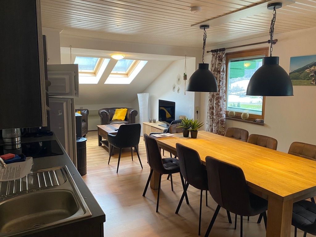 Großzügiger Essbereich mit langem Holztisch, schwarzen Pendelleuchten und Küche in wohnlichem Ambiente.