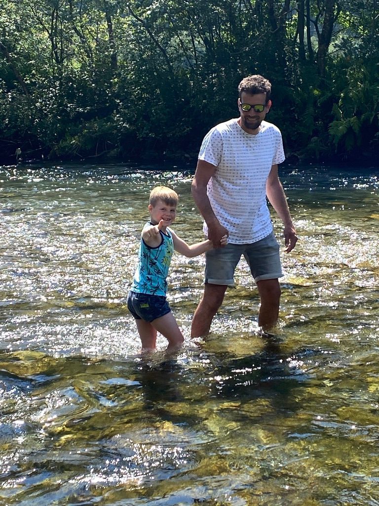 Een man en een kind staan ​​hand in hand in een rivier.