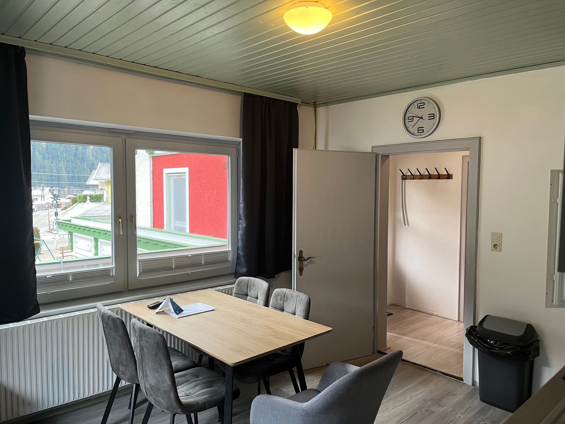 Essbereich mit Tisch, Stühlen, Fenster, Vorhängen und offener Tür.