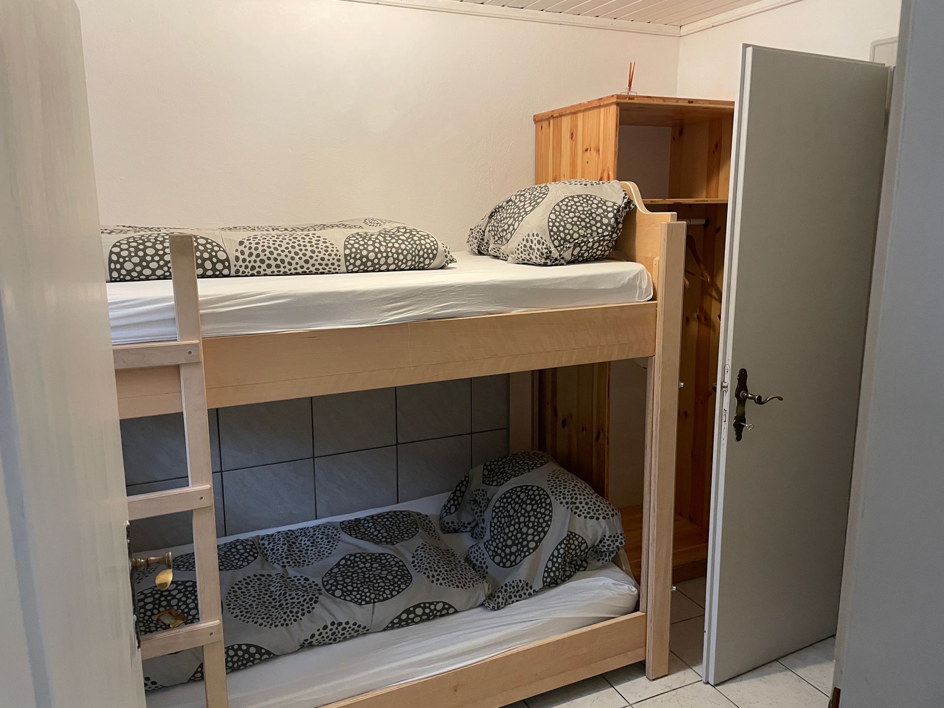 Etagenbetten in einem kleinen Zimmer mit hellen Wänden und einem Holzschrank.