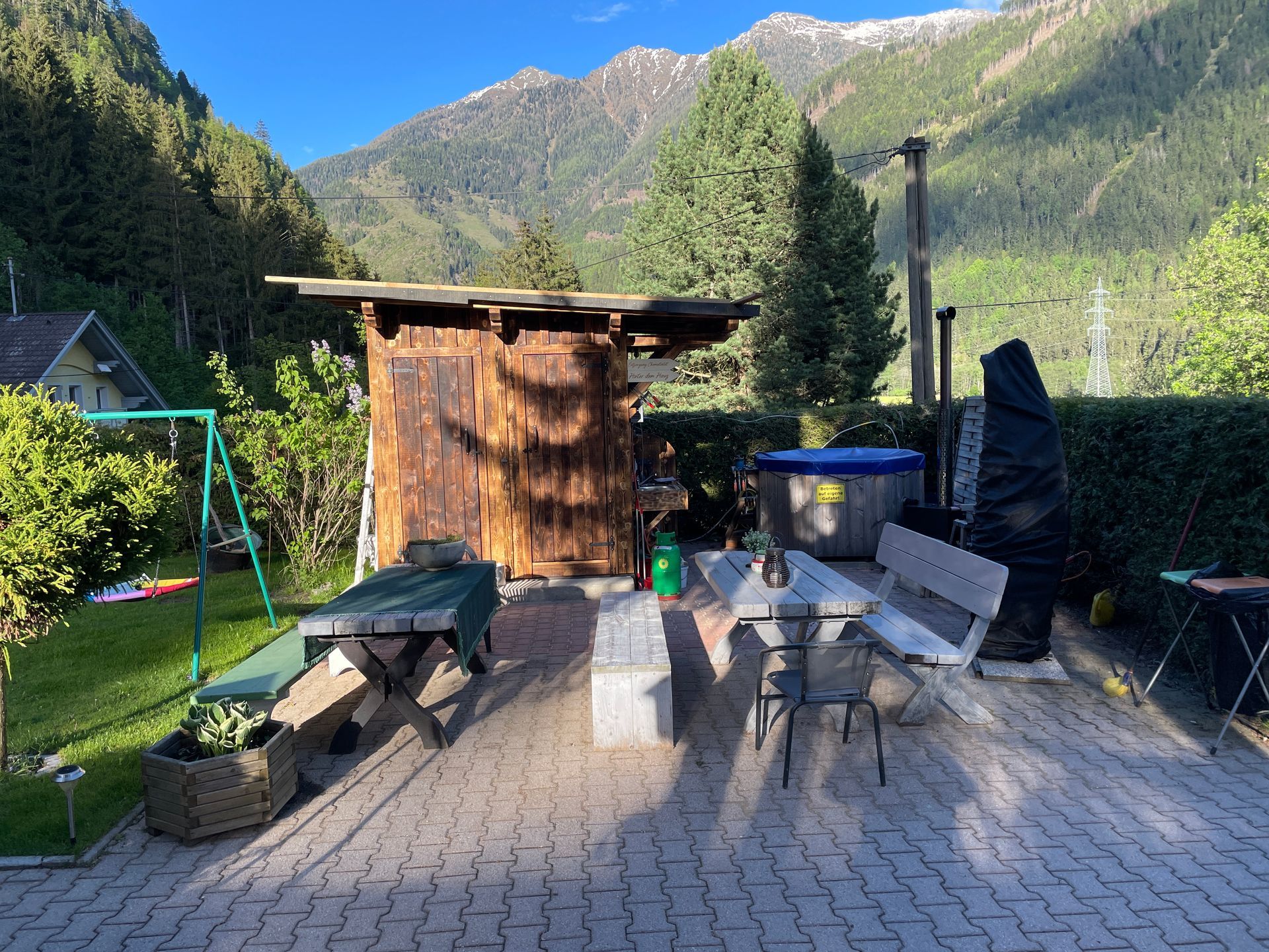 Een terras met een tafel en stoelen en een schuur met bergen op de achtergrond