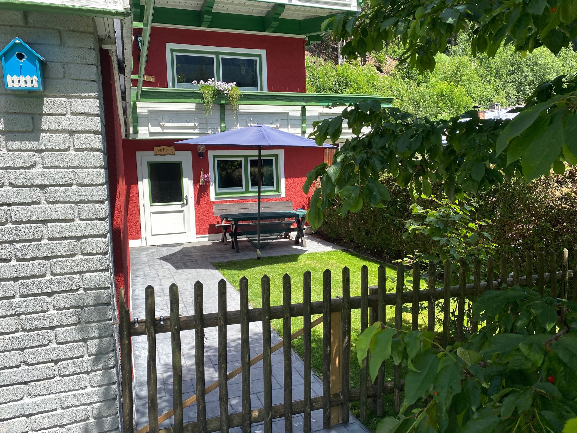 Een rood huis met een blauw vogelhuisje aan de zijkant