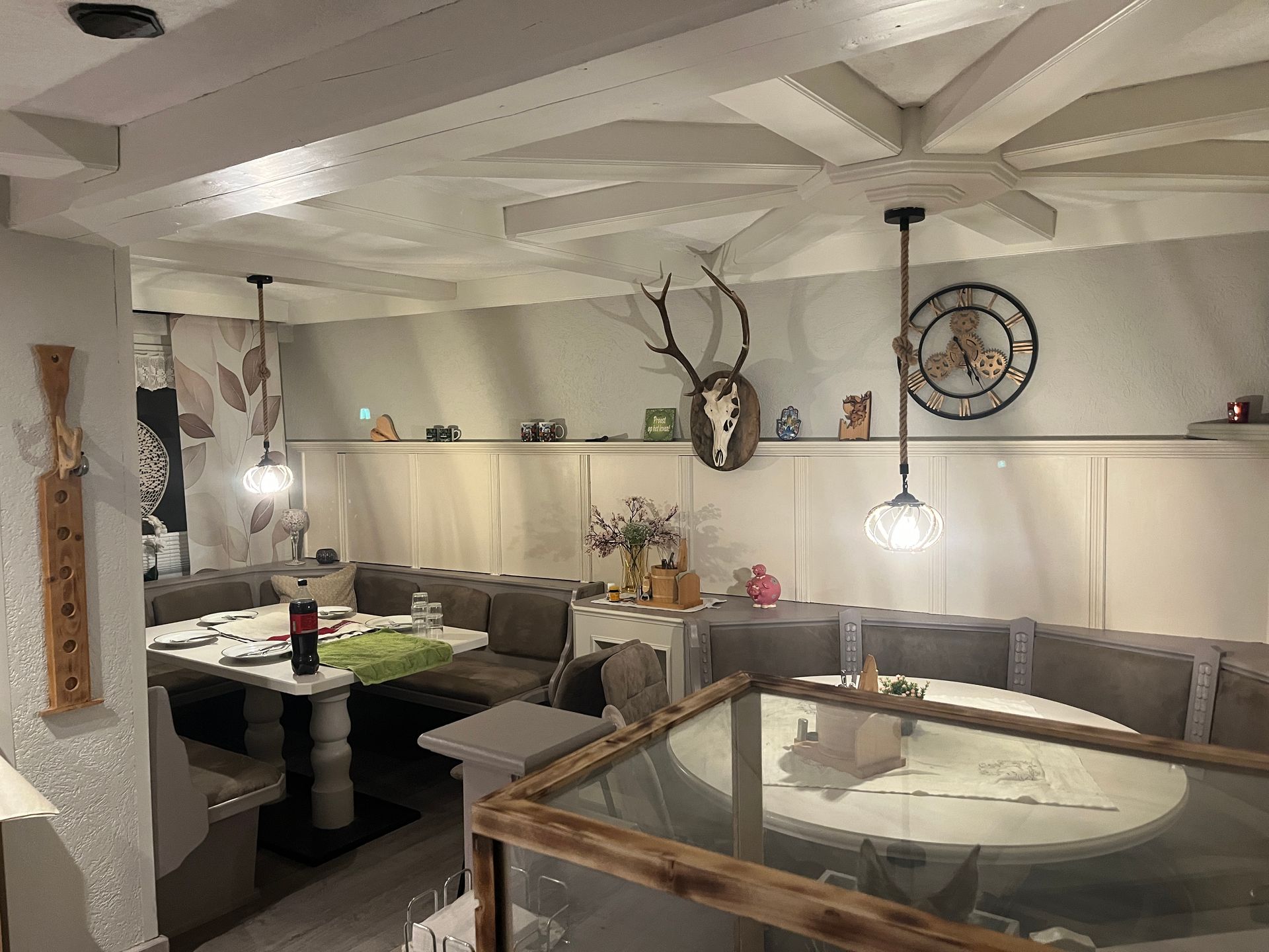 Gemütliches Esszimmer mit Sitznischen, dekorativen Deckenbalken, Geweihausstellung und Pendelleuchten.