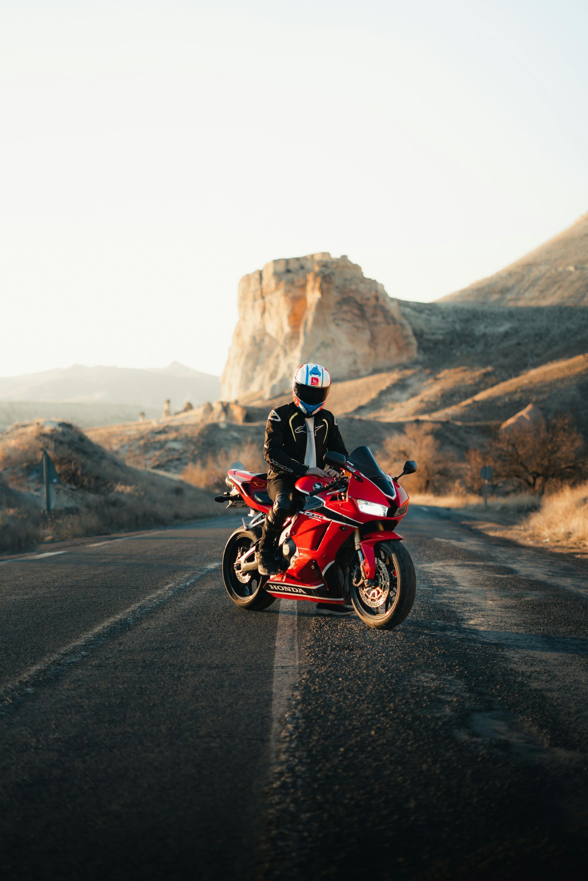 Rotes Motorrad auf einer Wüstenstraße, Fahrer mit Helm, im Hintergrund ein Berg.