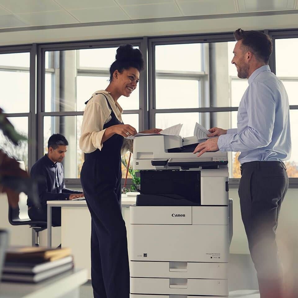 A man and a woman are standing in front of a canon printer.