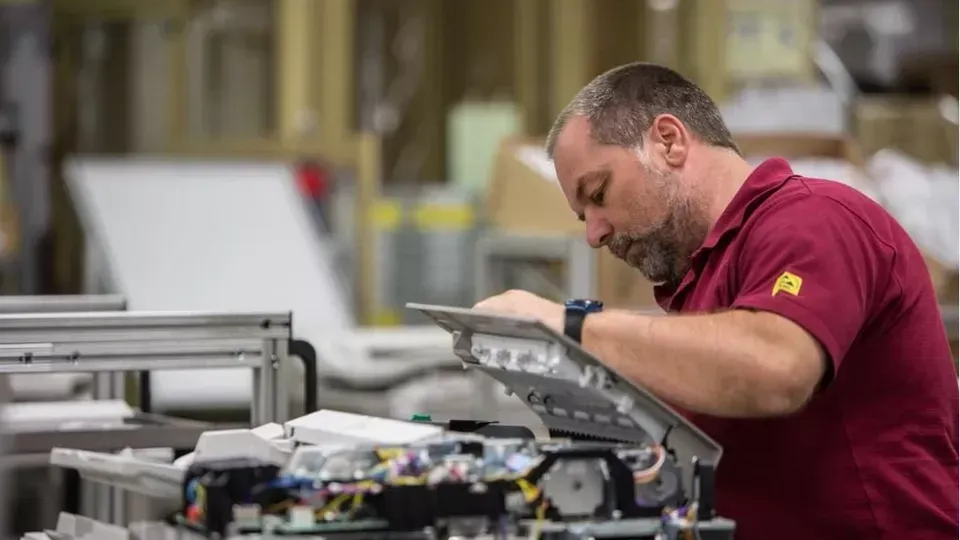 A man in a red shirt is working on a machine in a factory.