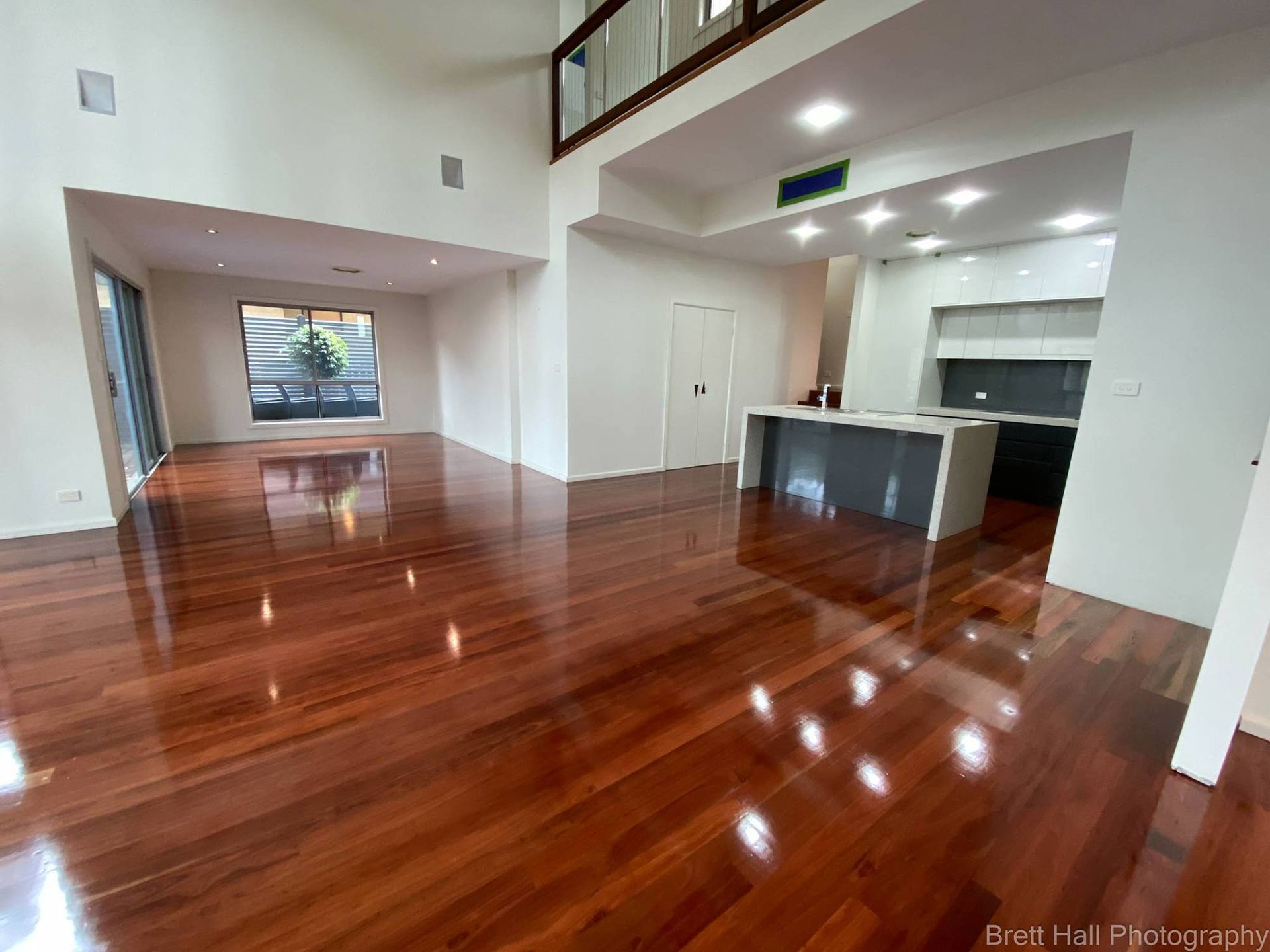 A Large Empty Room With Polished Hardwood Floors And A Kitchen — Brett Hall Floorsanding in Wauchope, NSW