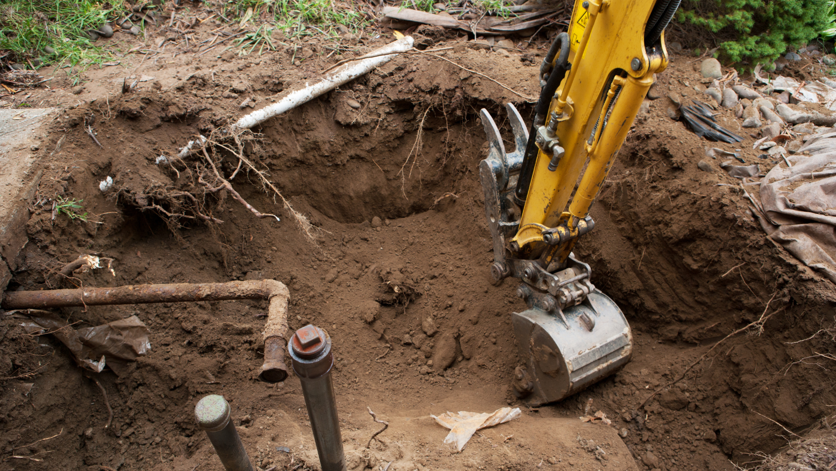 A yellow excavator is digging a hole in the ground to remove an underground storage tank