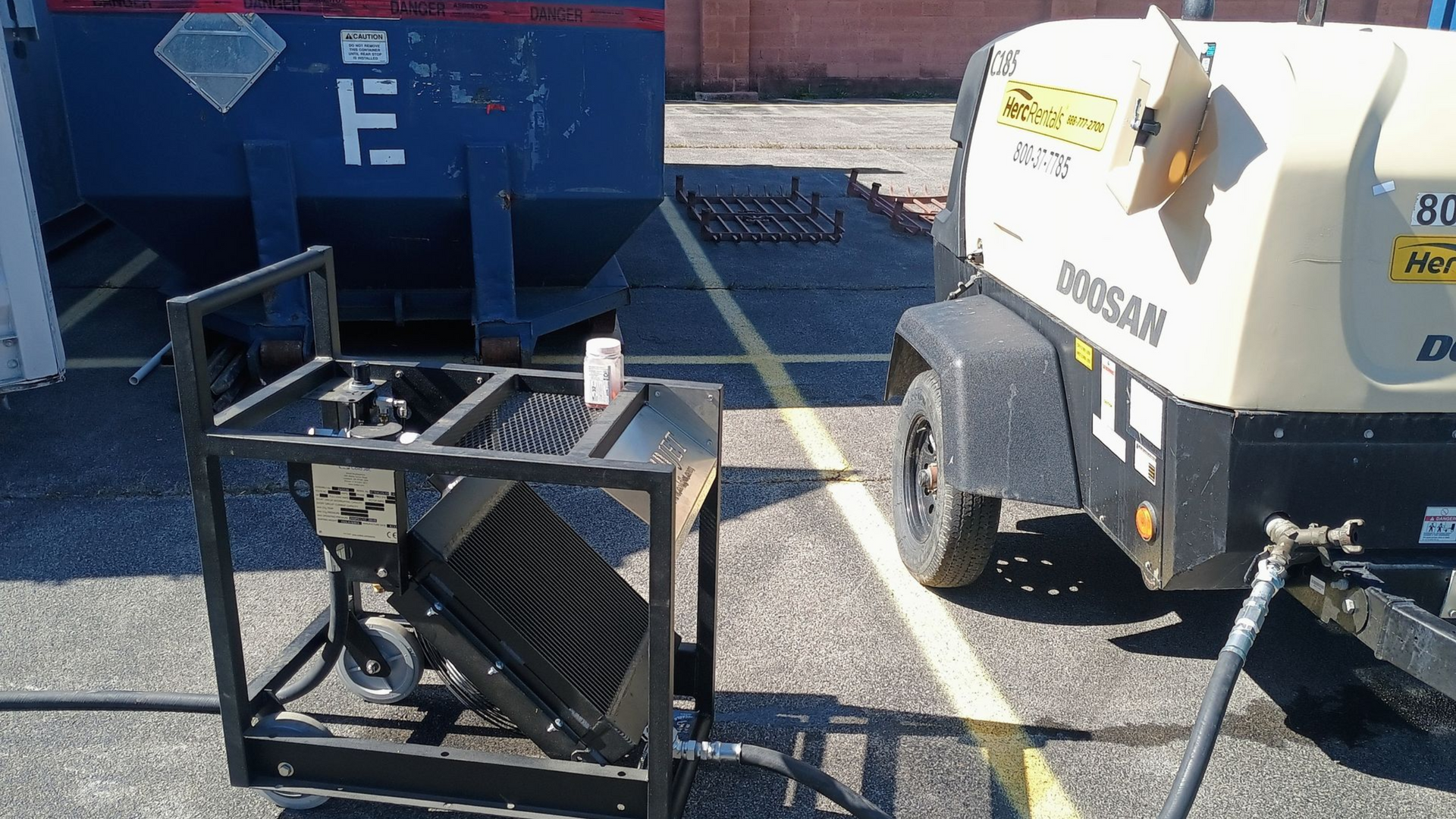 Portable dry ice blaster  in a gravel lot beside a blue dumpster and a white service truck