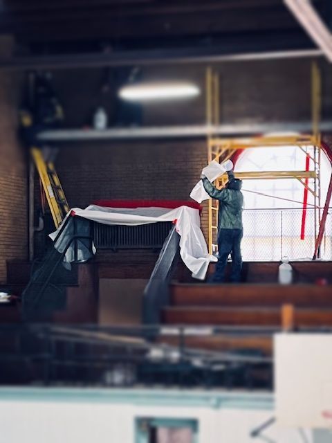 Person in a warehouse lifting a red-and-white draped beam with a yellow hoist