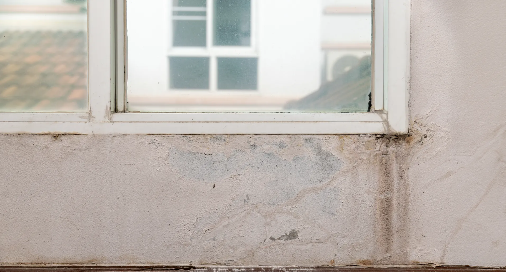 Window frame with water damage on the wall below. The wall is a textured white.
