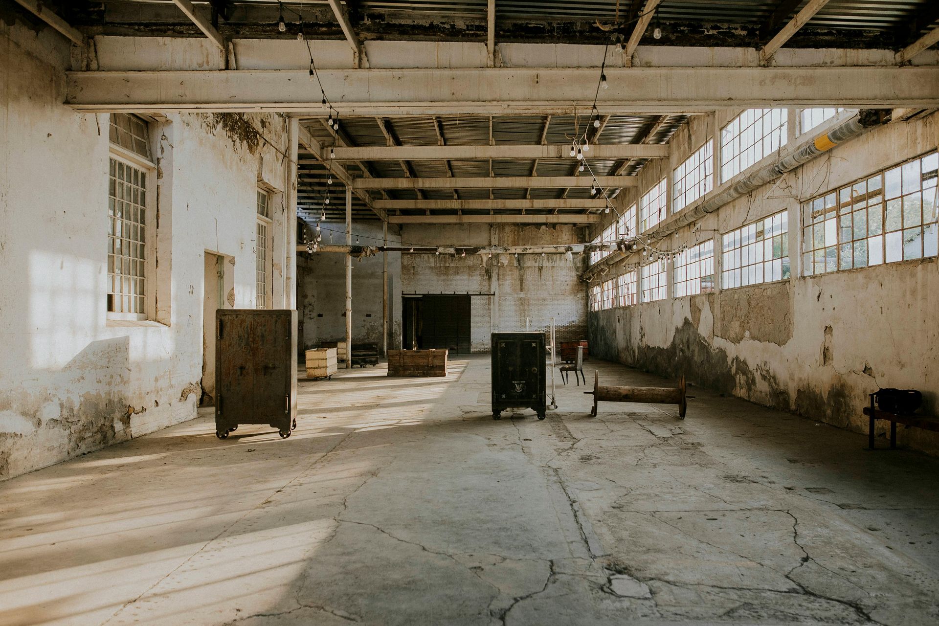 Abandoned warehouse interior with cracked floor, peeling walls, and broken windows letting in light