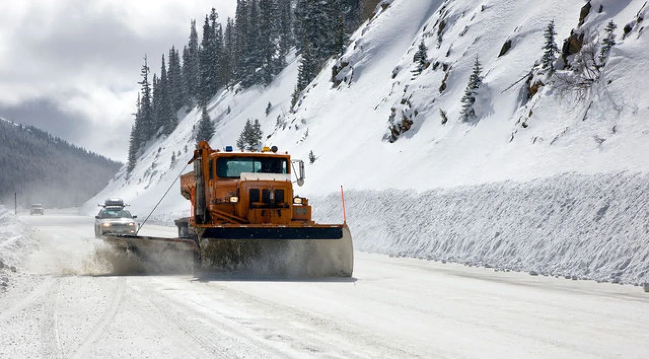 Orange snowplow clearing a snowy mountain road beside high snowbanks