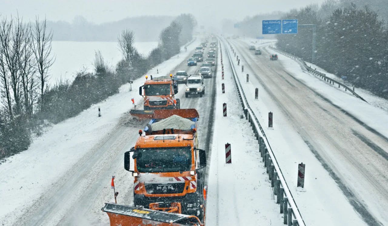 Orange snowplows clearing a snowy highway in a winter storm