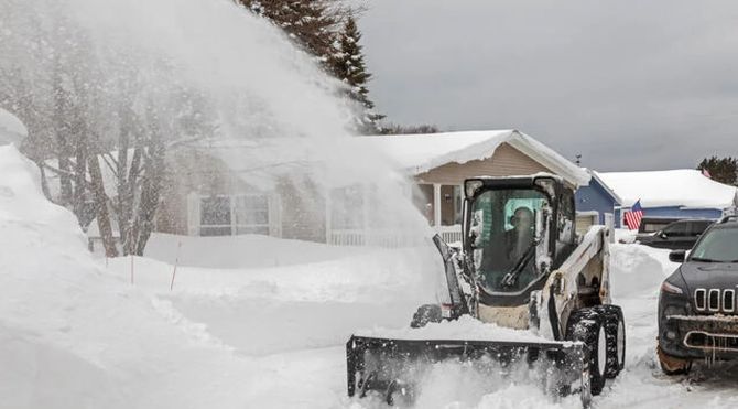Snow blower clearing a driveway beside a parked SUV and house in a snowy neighborhood