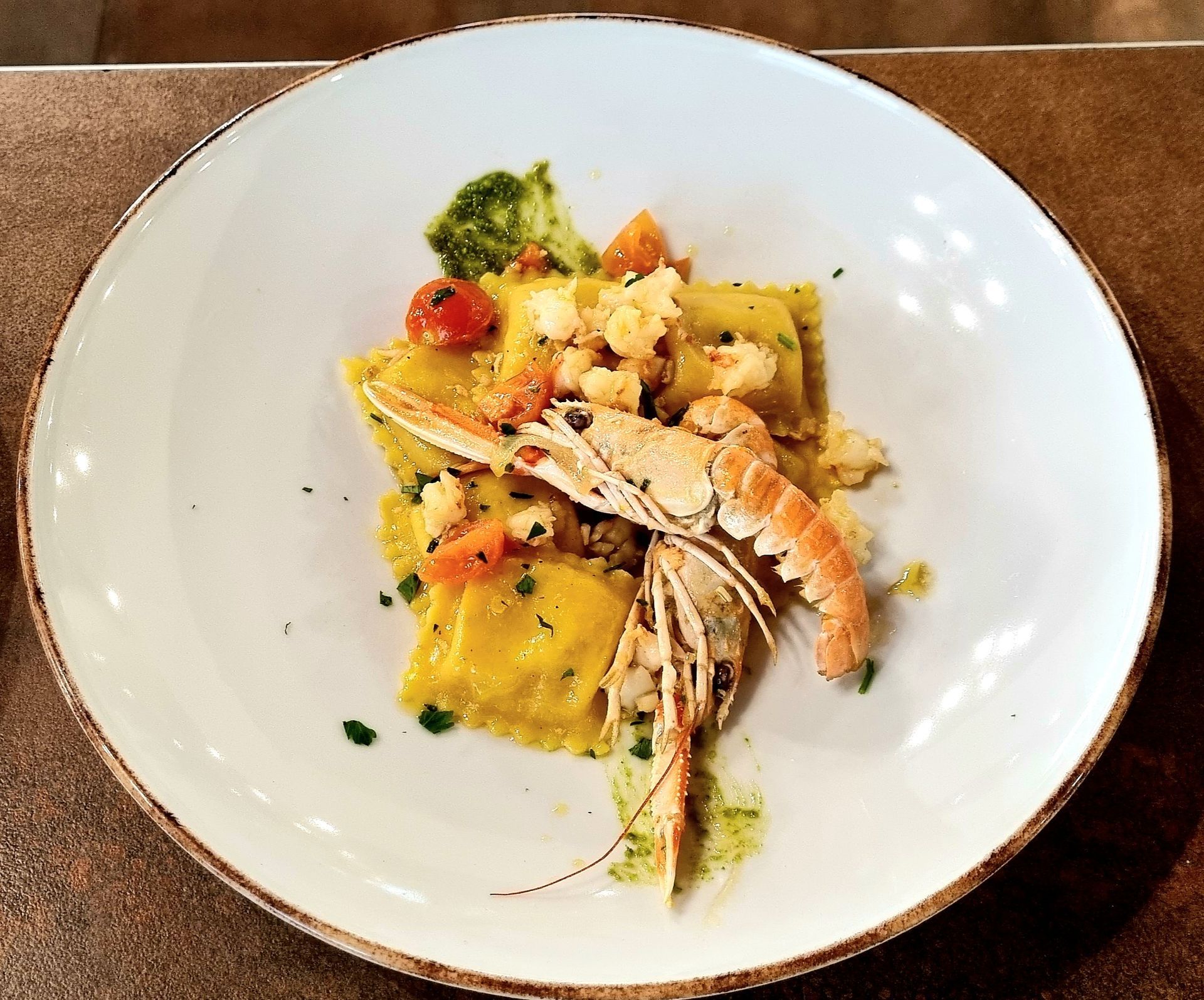 Piatto di pasta con gamberi grandi, pomodori e pesto su un piatto bianco.