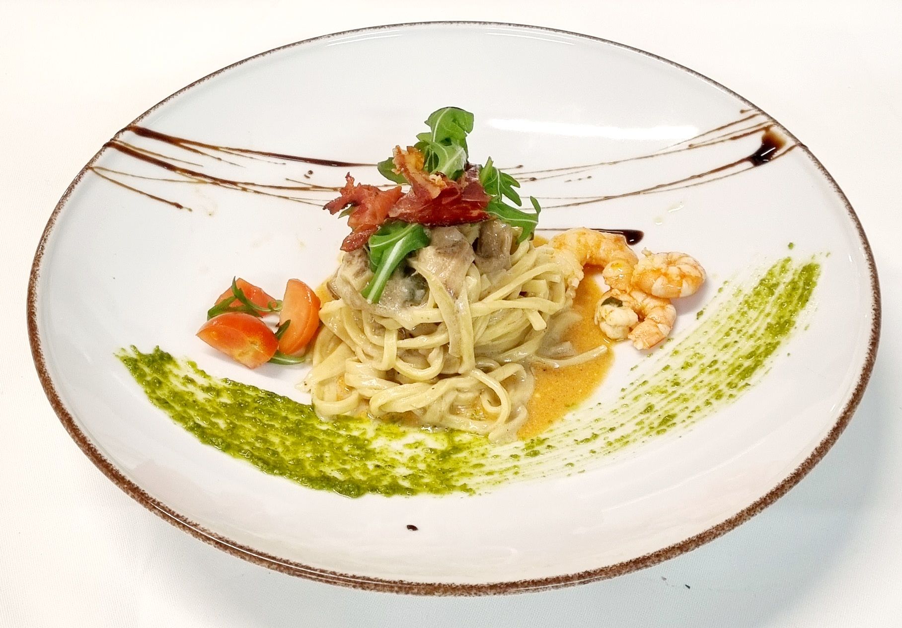 Piatto di pasta con pesto, gamberi, pomodori e guarnizione, su un piatto bianco.
