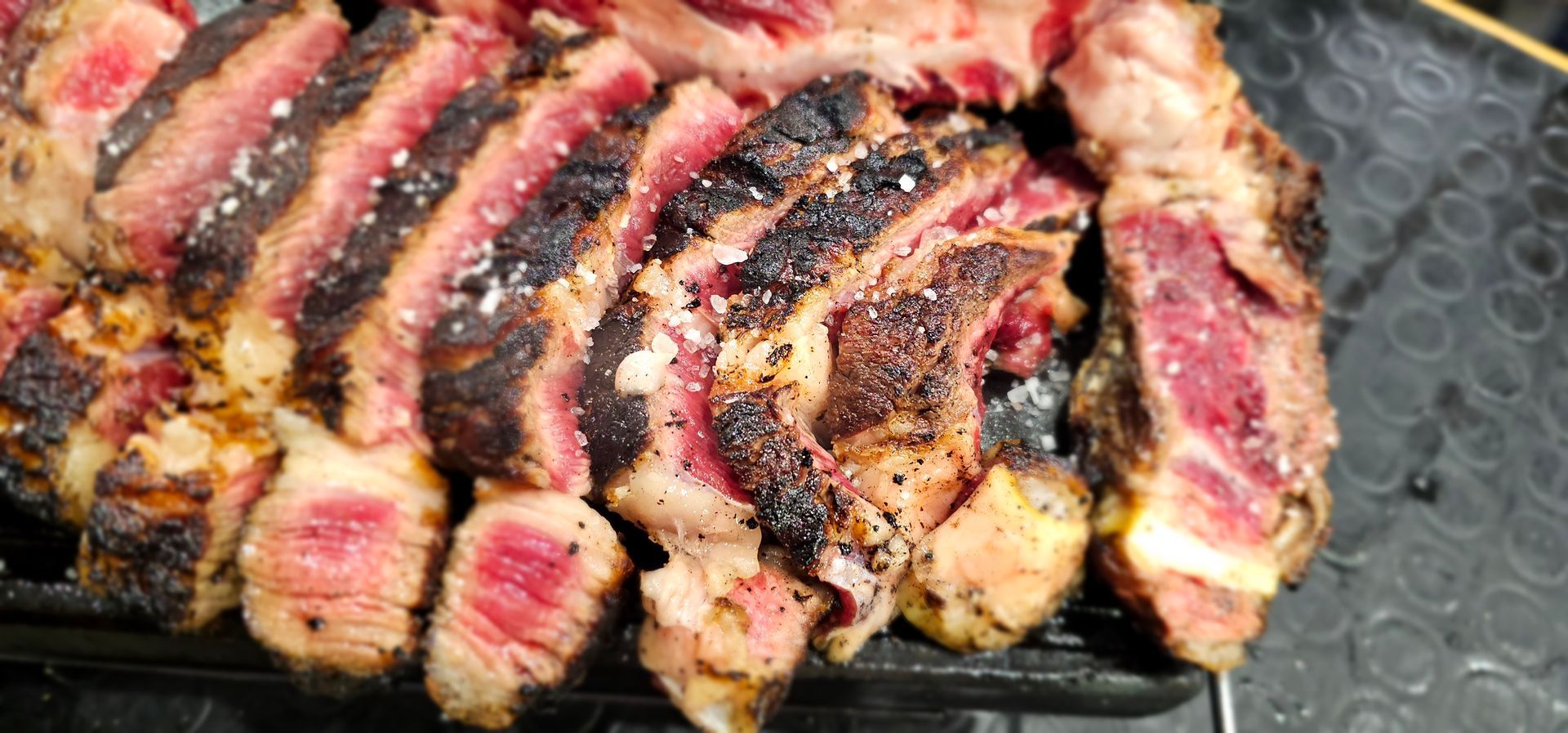 Bistecca tagliata a fette, cotta al sangue e cotta sulla griglia, con crosta bruciacchiata e interno rosa.