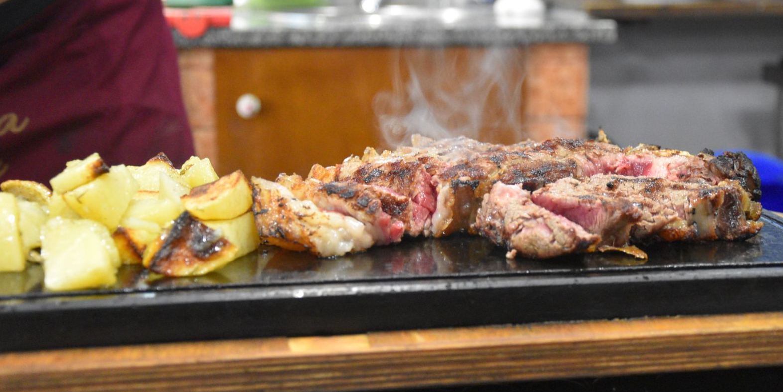 Bistecca tagliata a fette e scottata alla griglia, al sangue, con interno rosa e crosta scura, cosparsa di sale.