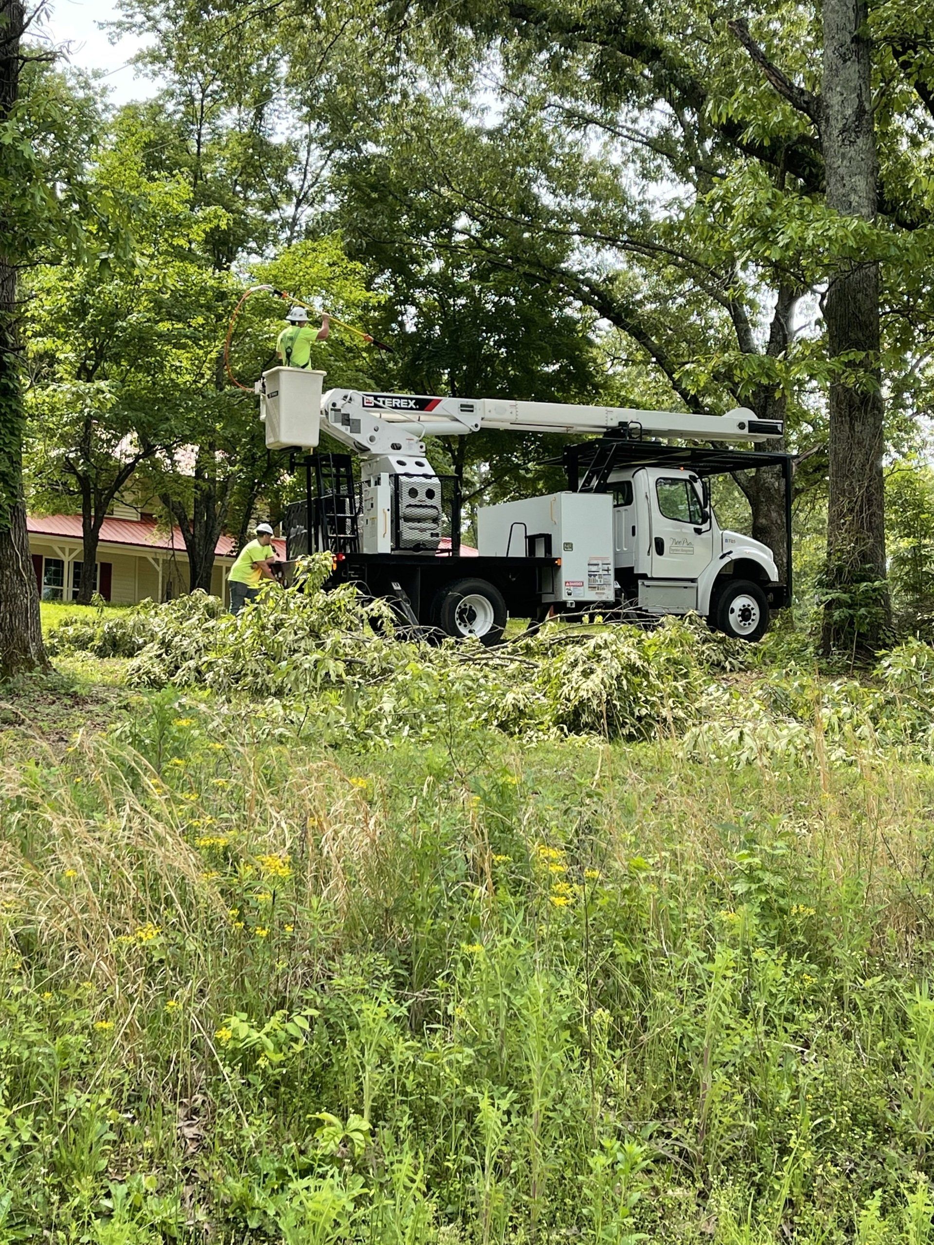 White utility truck with raised bucket arm parked in a green wooded area