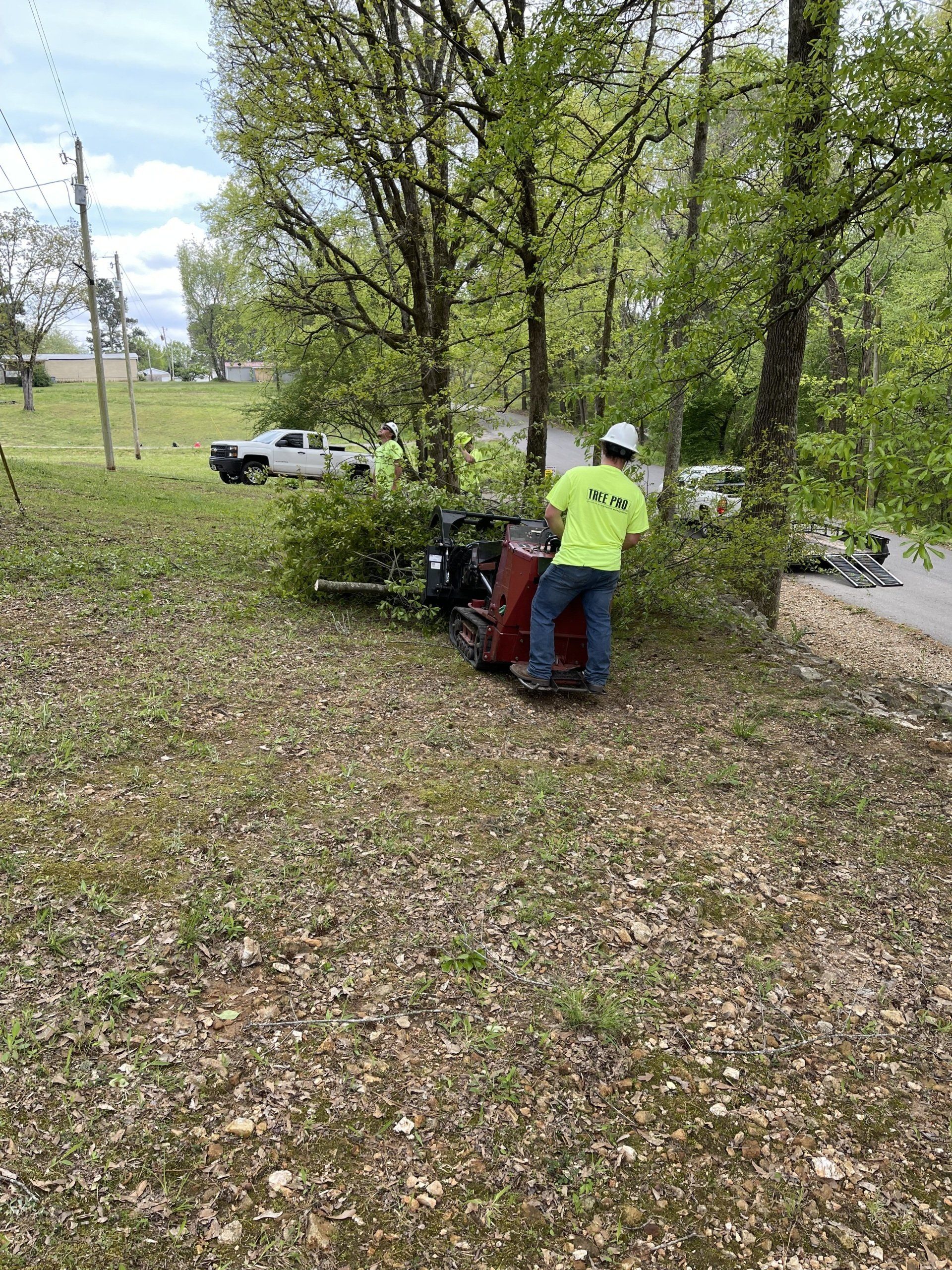 Two people in neon jackets tending a red machine under trees in a grassy park.