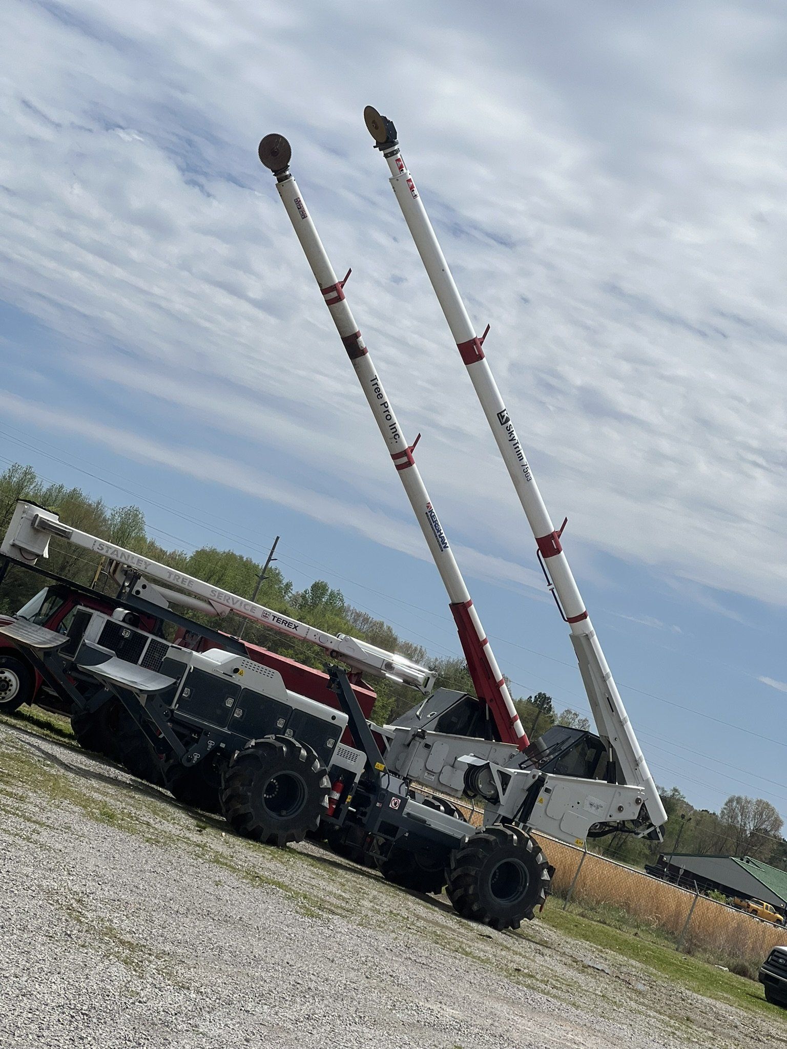 Two raised crane booms on a work truck at a gravel site under a cloudy sky
