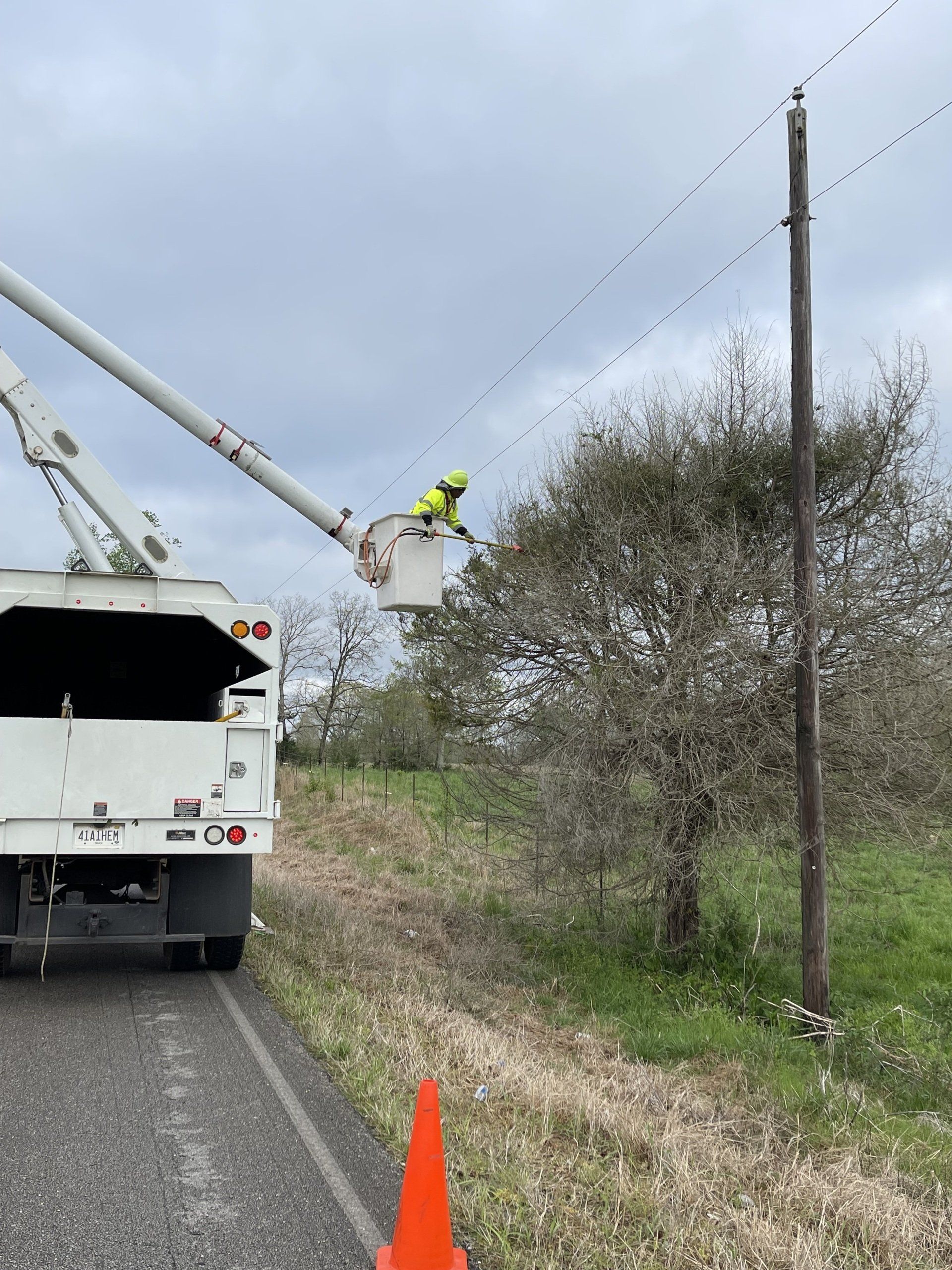 Utility worker on a bucket truck repairing power lines beside a rural road under a cloudy sky