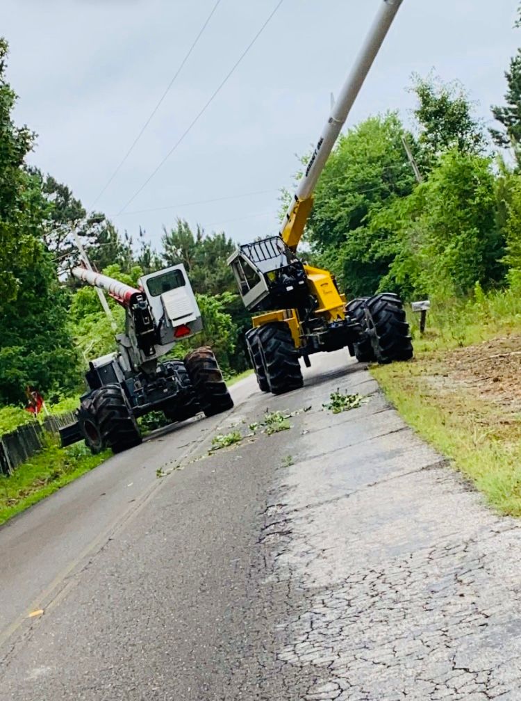 Two utility trucks on a damaged road, one with a raised boom near fallen power lines.