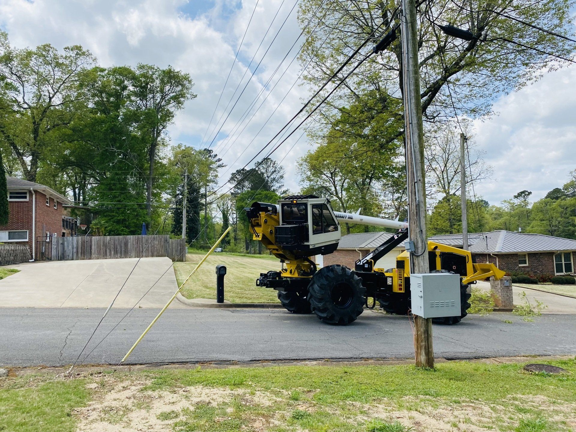 Yellow utility machine on a residential street beside power lines and a utility pole