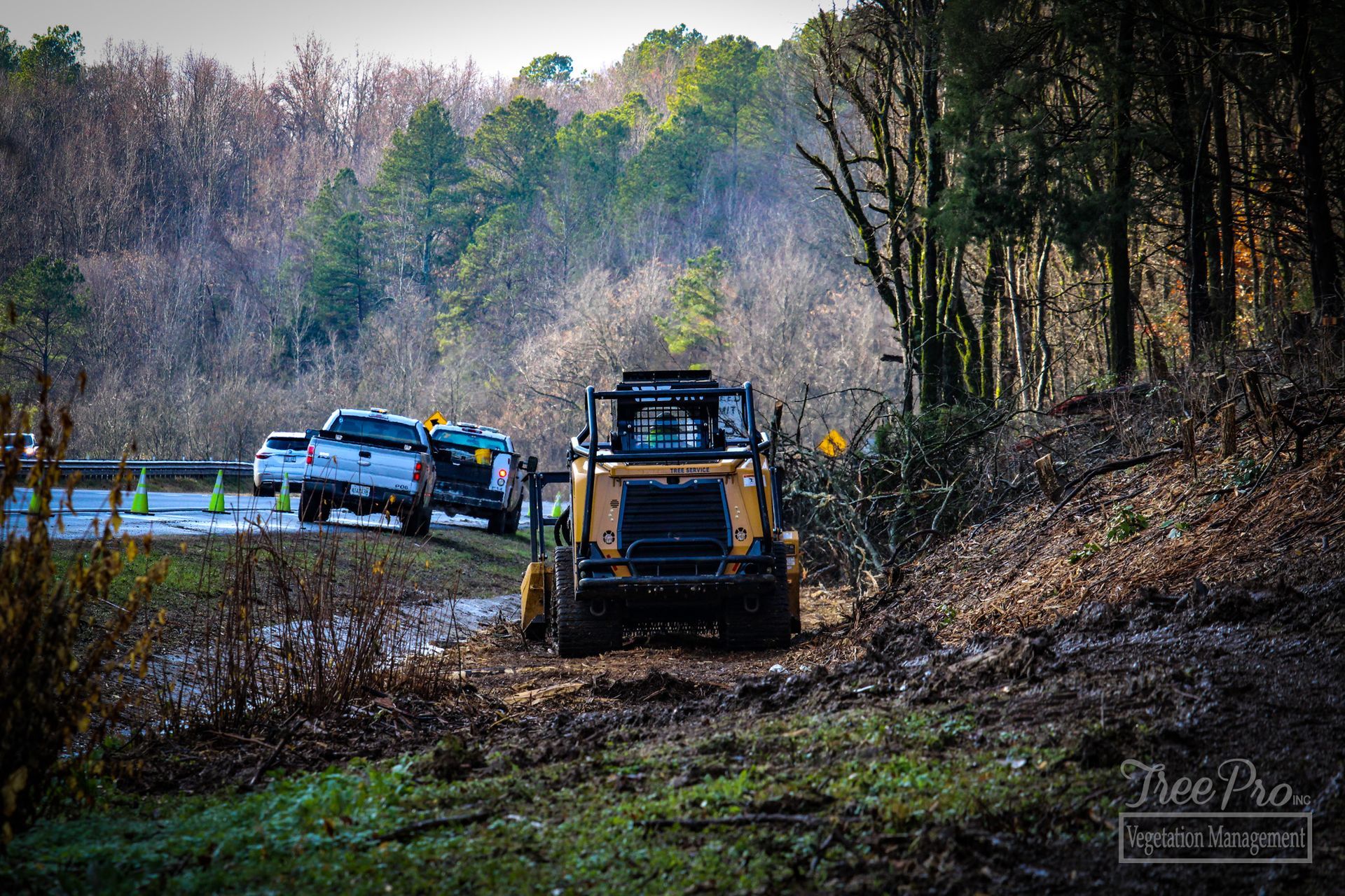 Yellow excavator on a muddy woodland path with two vehicles near a forest road