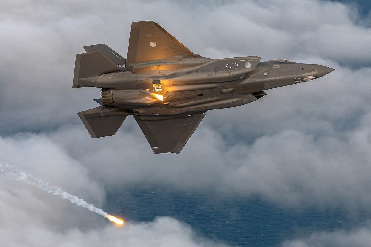 A fighter jet is flying through the clouds with a rocket coming out of it.