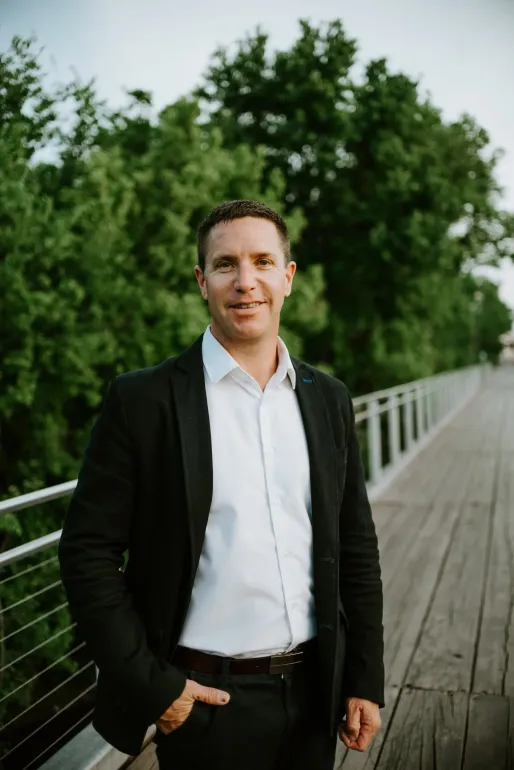 A man in a suit and white shirt is standing on a bridge.
