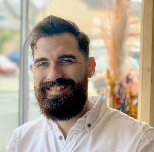 A man with a beard is wearing a white shirt and smiling.