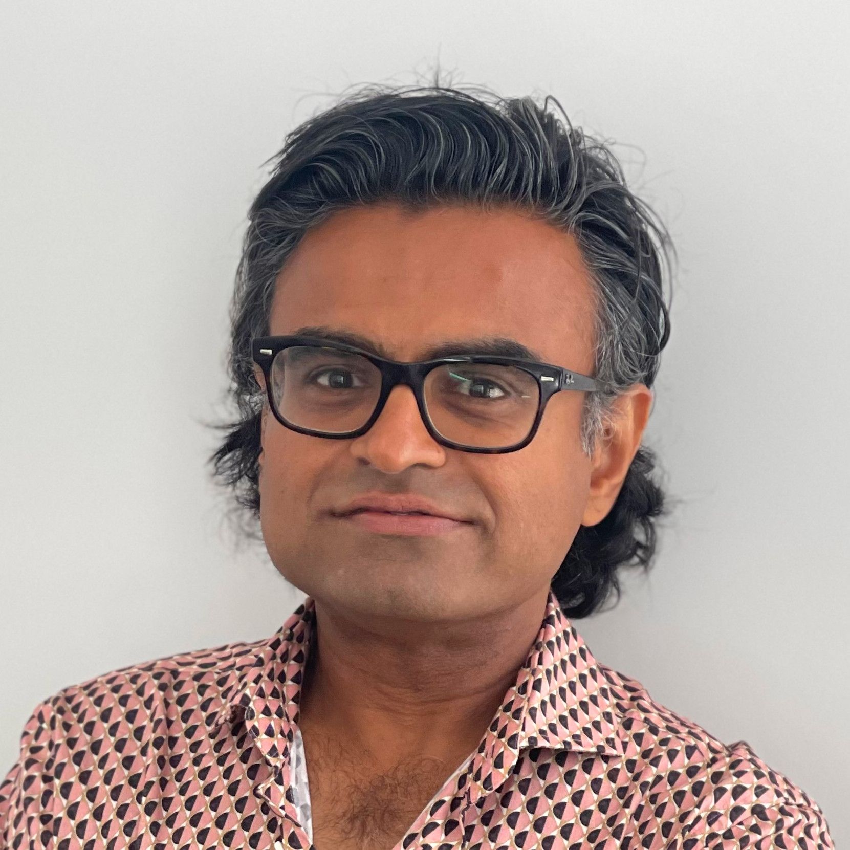 Our doctor wearing glasses and a pink shirt looks at the camera