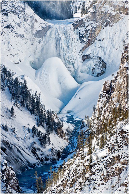 A waterfall is surrounded by snow covered mountains and trees