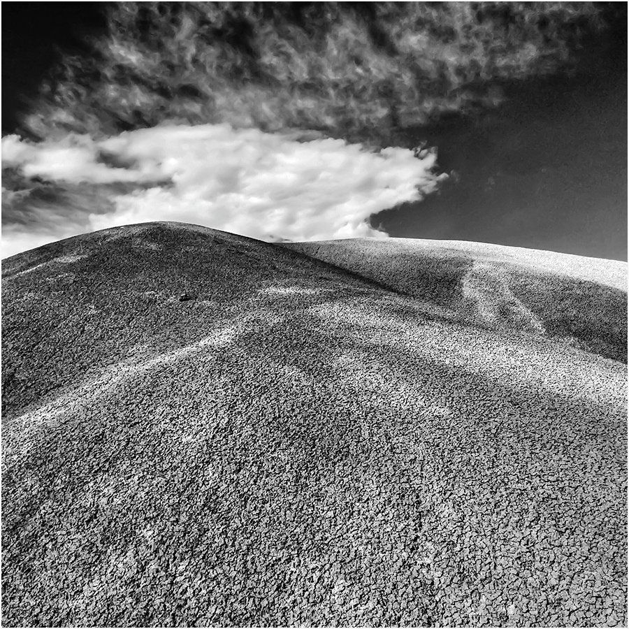 A black and white photo of a hill with clouds in the sky