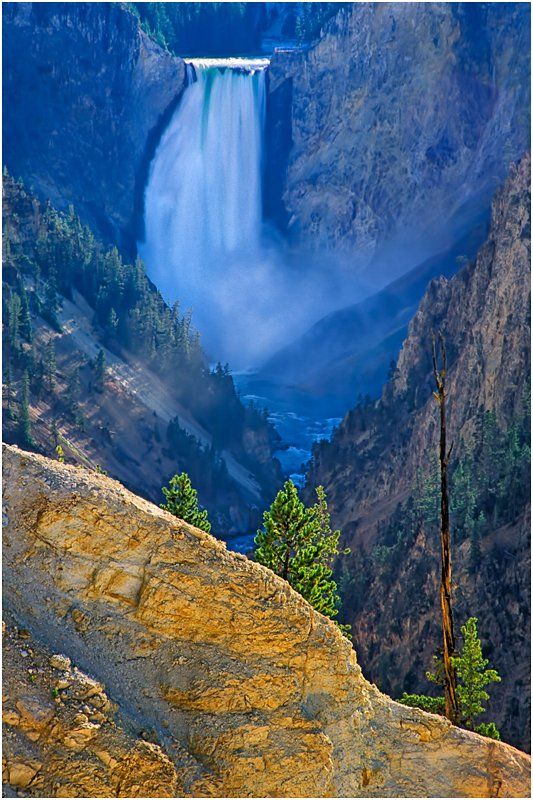 A waterfall is surrounded by mountains and trees in the middle of a canyon.
