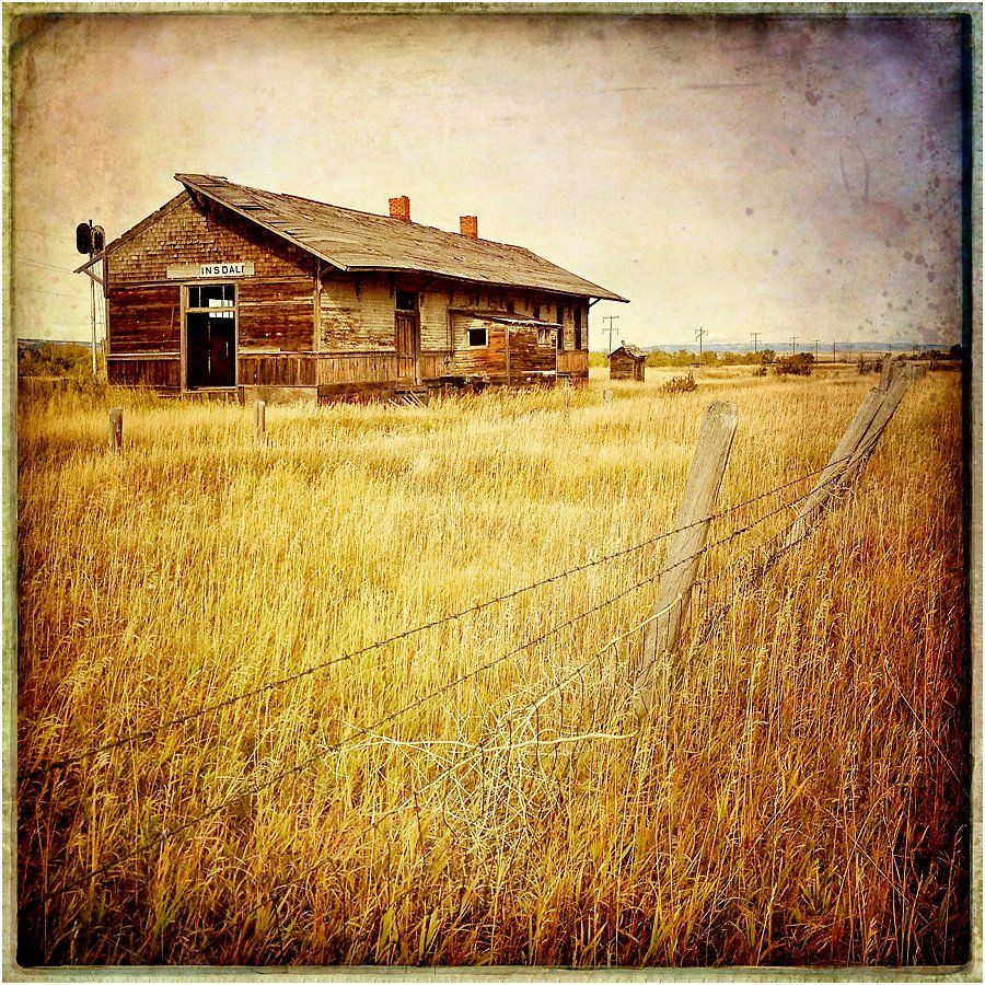 An old building in the middle of a field with a barbed wire fence around it