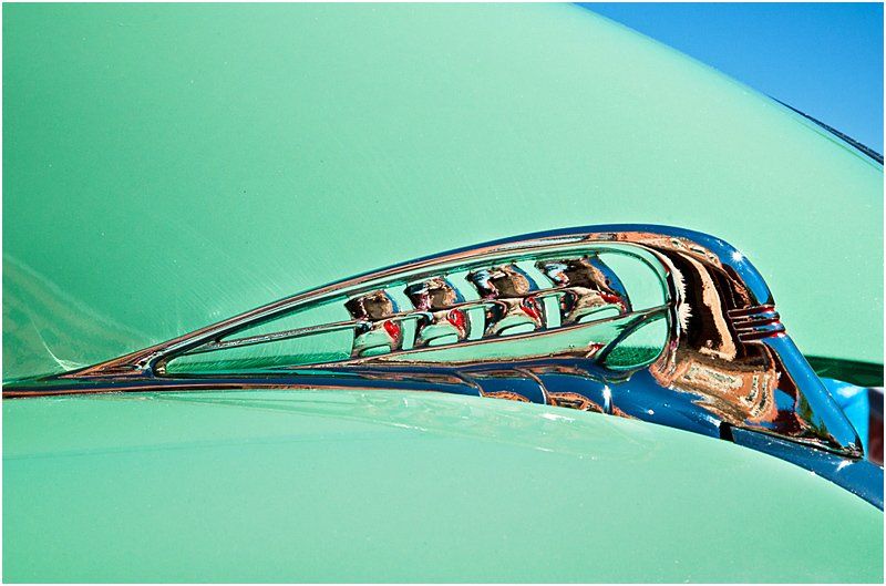 A close up of a green car with a chrome emblem on the hood.