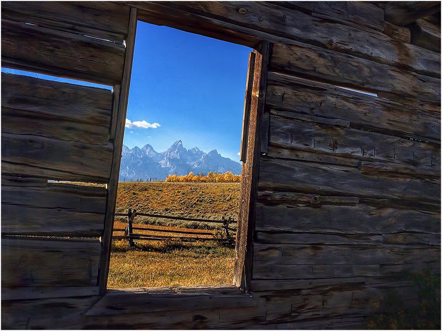 A view of mountains through a window of a log cabin