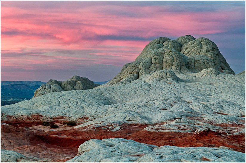 A mountain in the middle of a desert with a pink sky in the background.