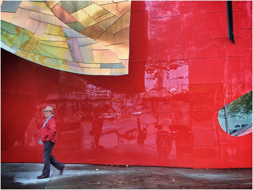 A woman in a red jacket is walking in front of a red wall.